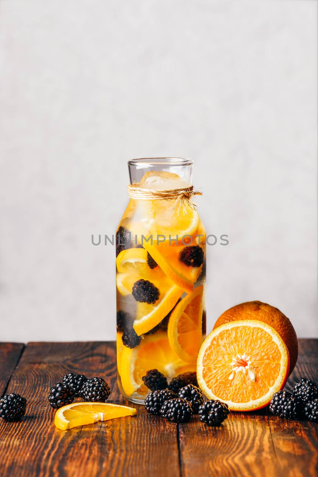 Bottle of Detox Water Infused with Sliced Raw Orange and Fresh Blackberry. Ingredients on Wooden Table.