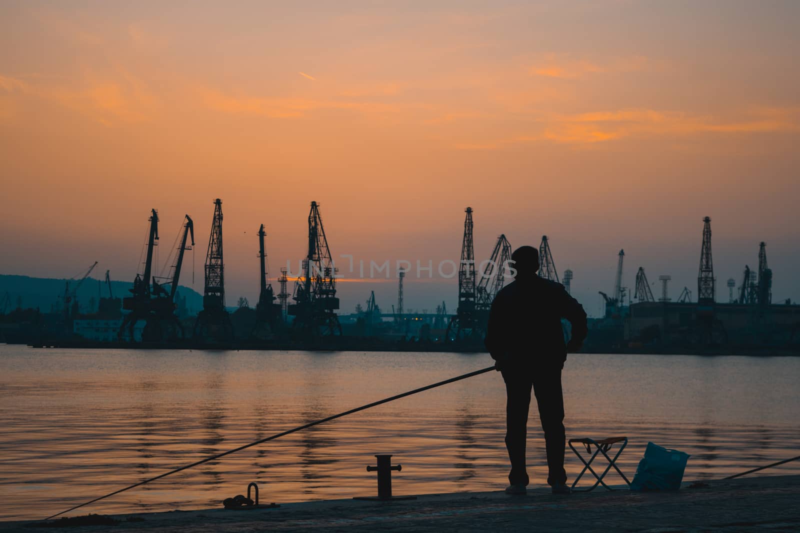 Fisherman silhouette at the docks in the harbor at golden sunset hour. by justbrotography