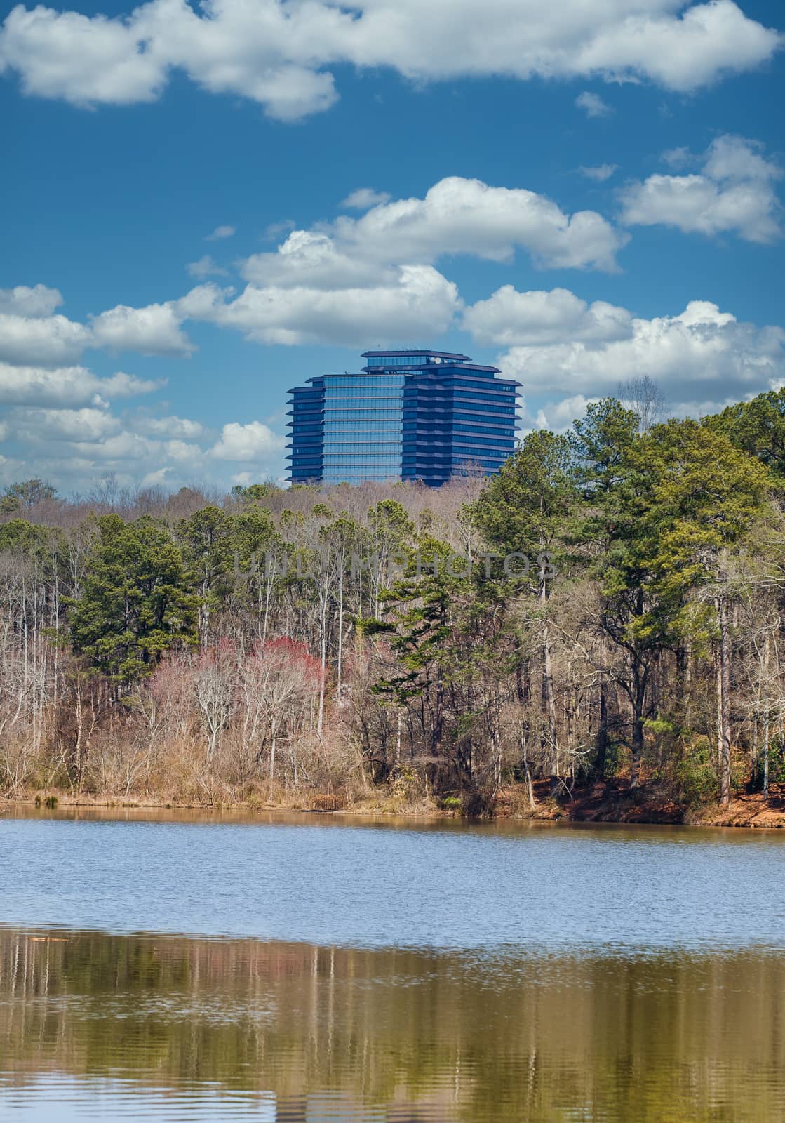 A black office tower in distance beyond a calm lake in winter with a reflection