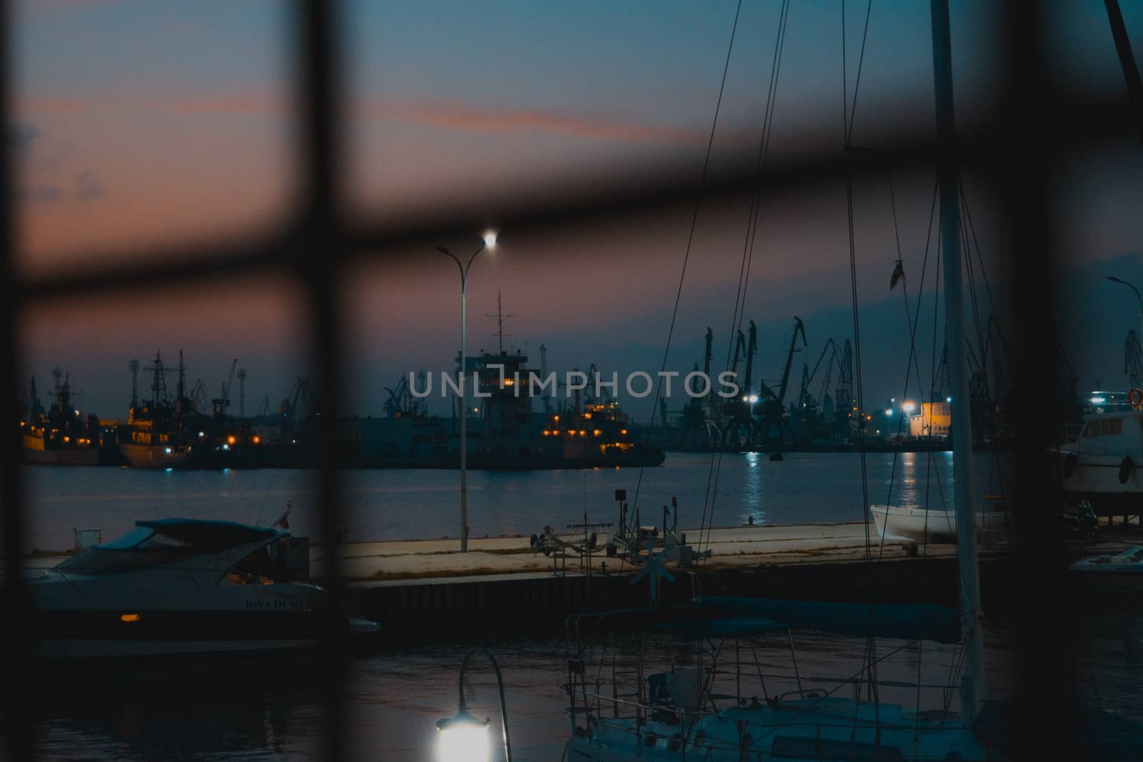 Stunning night view through a metal fence with a yacht and some ships for background. by justbrotography