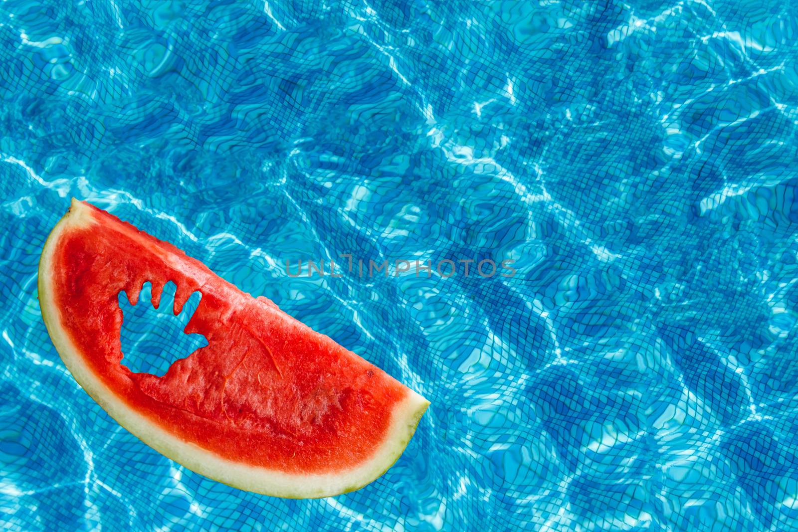 In the pool with blue water, a slice of watermelon with a carved children's hand swims. Copy space. View from above