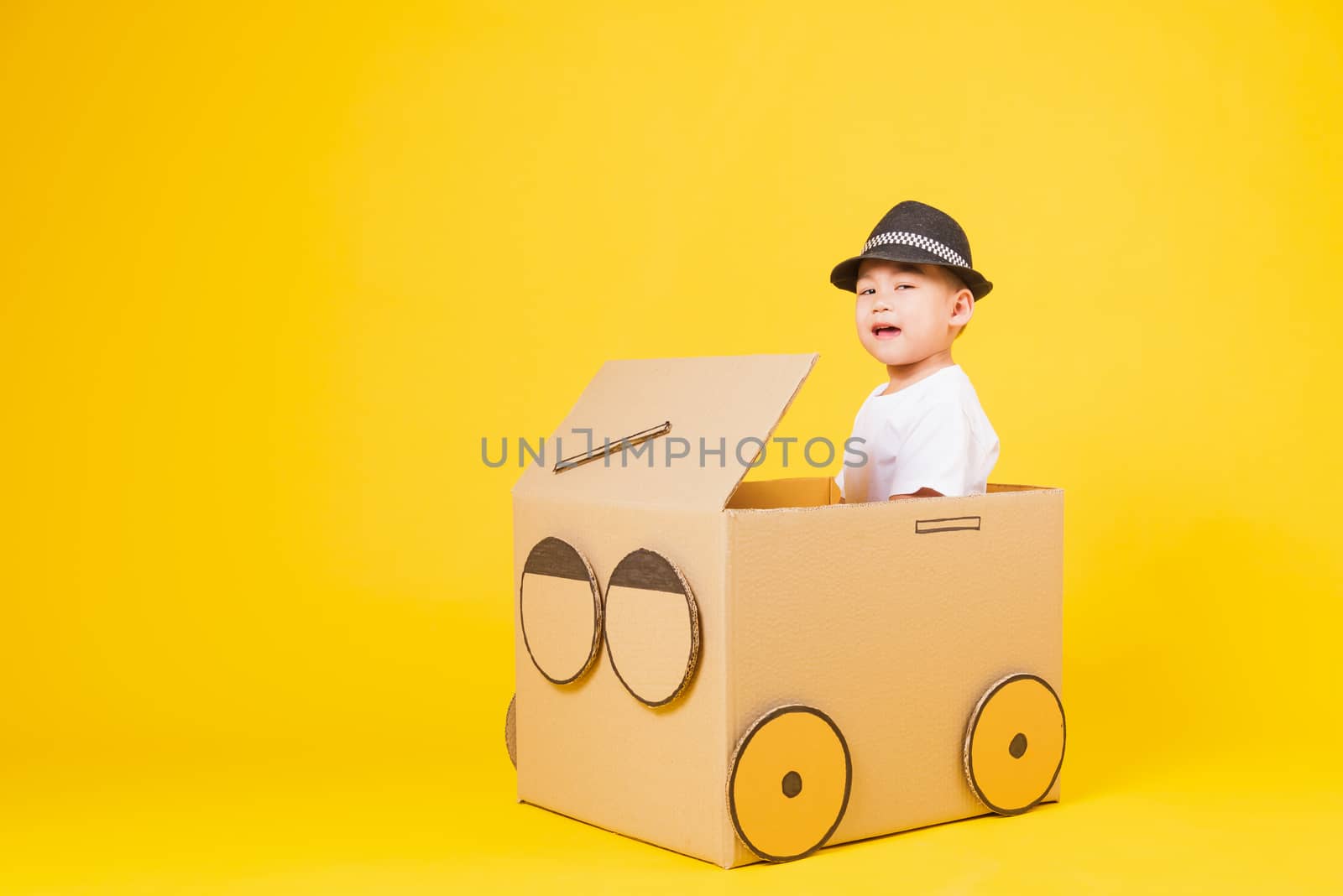 Portrait happy Asian cute little children boy smile so happy wearing white T-shirt driving car creative by cardboard, studio shot on yellow background with copy space