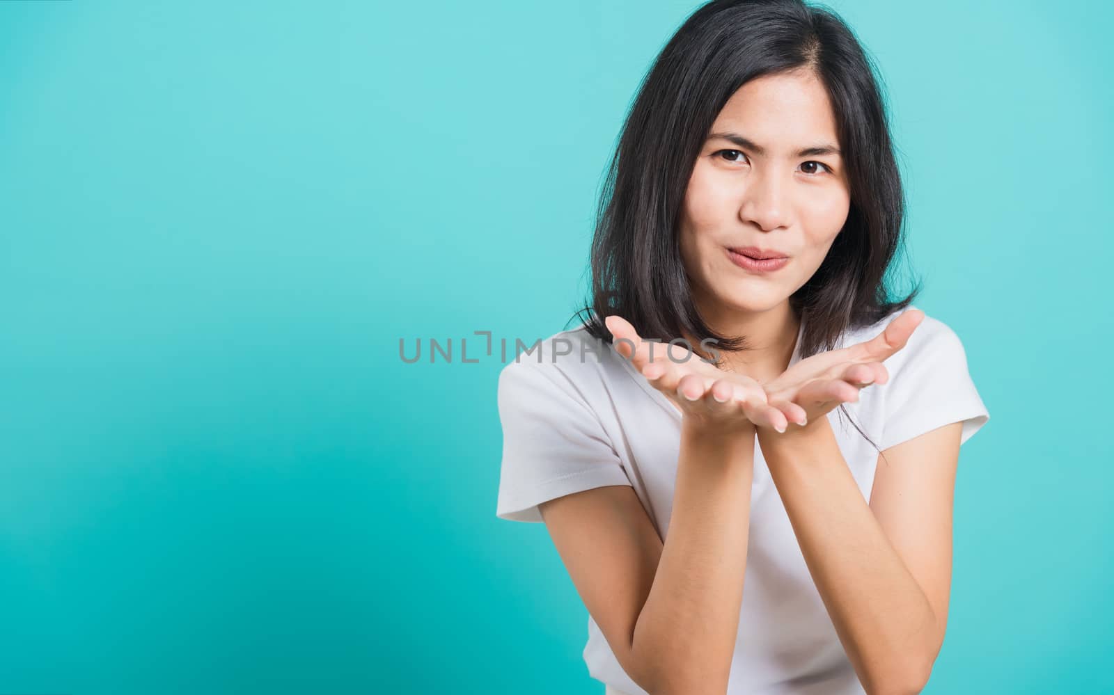 Portrait happy Asian beautiful young woman smile standing wear a white t-shirt, She blowing air kiss something on palms, studio shot on blue background with copy space for text