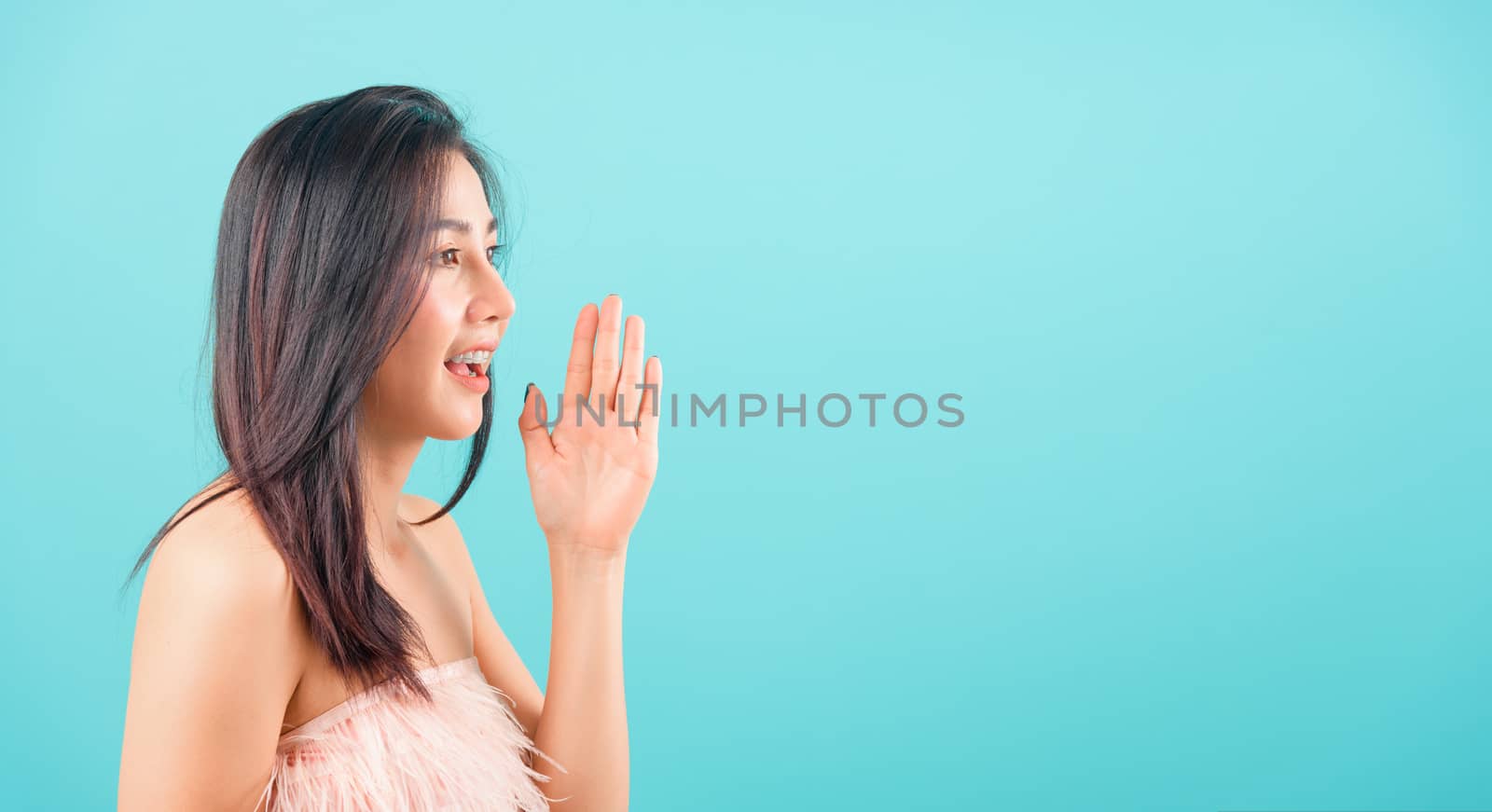 Portrait asian beautiful woman smiling and hand beside mouth telling somthing her eyes looking out on blue background, with copy space for text