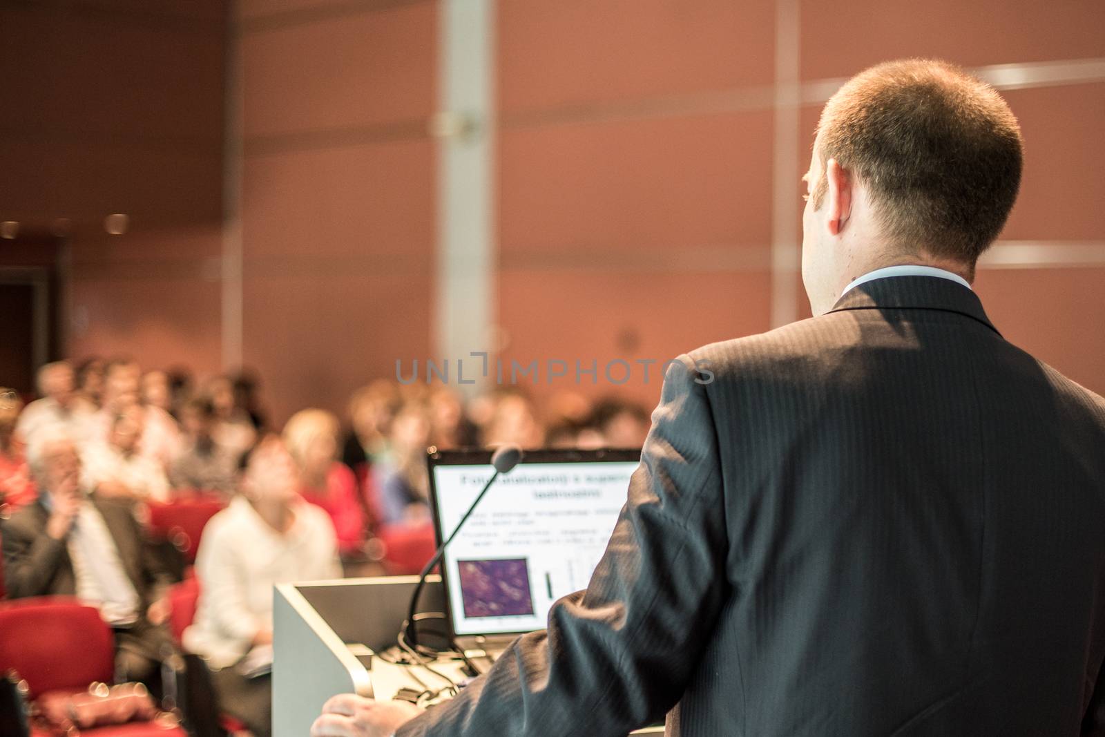 Speaker giving a talk on corporate business conference. Unrecognizable people in audience at conference hall. Business and Entrepreneurship event.