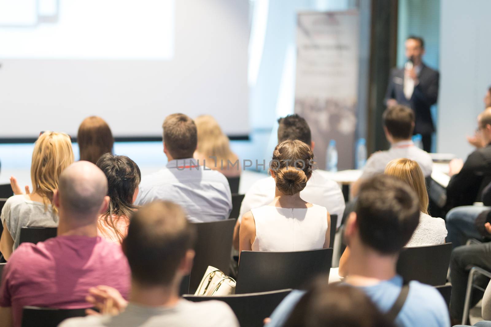 Male speaker giving a talk in conference hall at business event. Audience at the conference hall. Business and Entrepreneurship concept. Focus on unrecognizable people in audience.