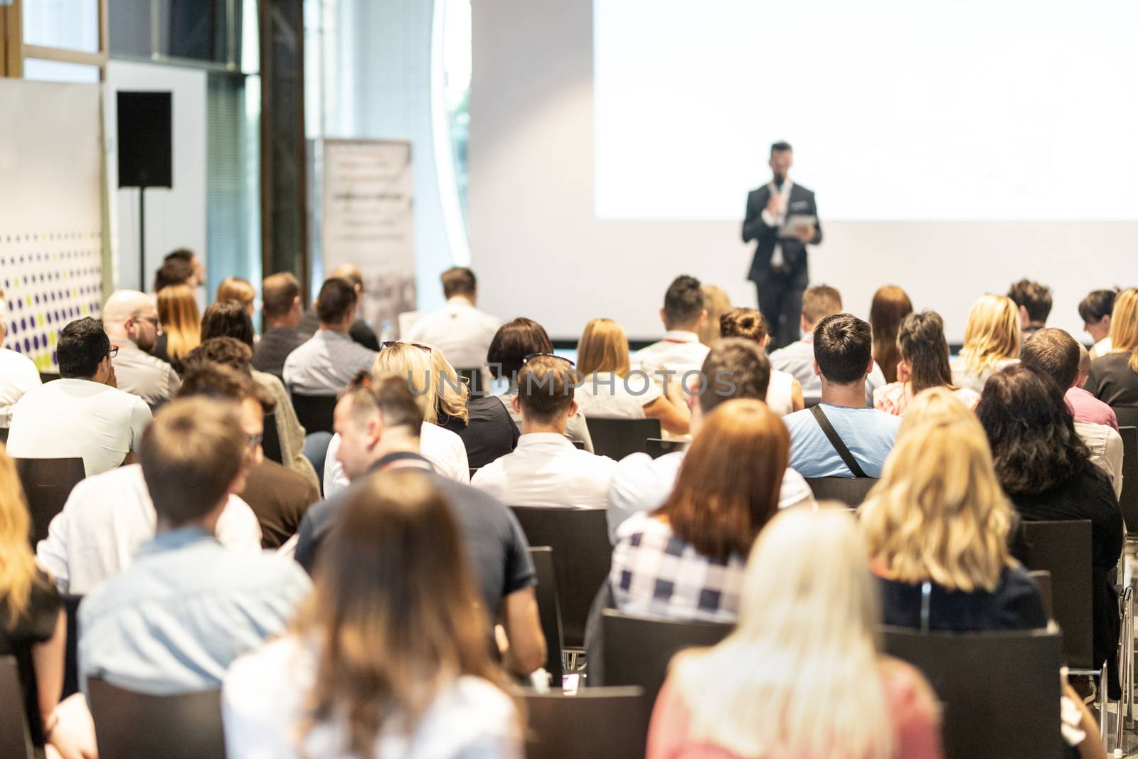 Male speaker giving a talk in conference hall at business event. Audience at the conference hall. Business and Entrepreneurship concept. Focus on unrecognizable people in audience.