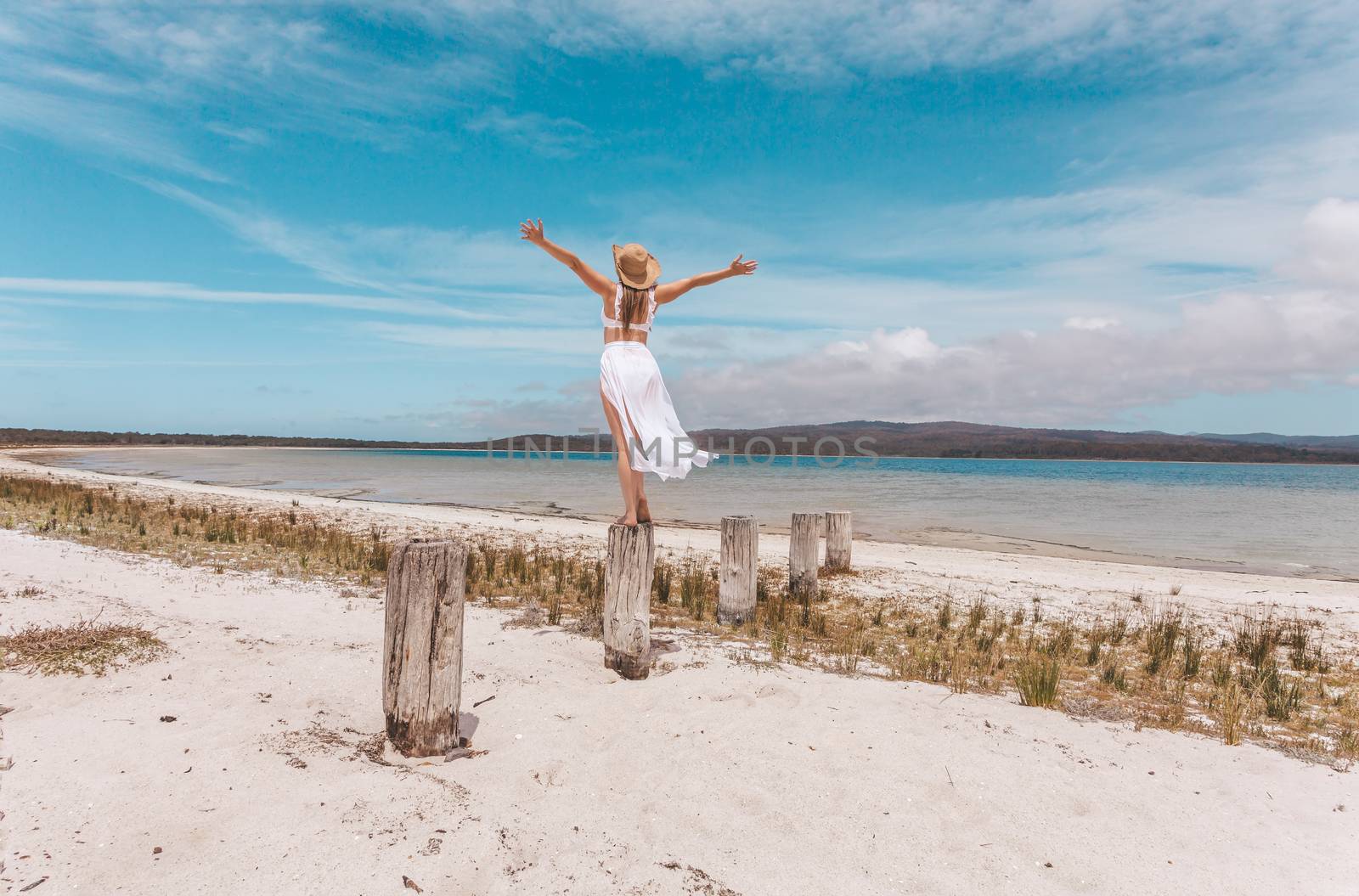 A female on vacation at the beach wearing a white swimsuit with sarong skirt,arms outstretched feeling free, alive, full of joy.  Australian travel, tourism or emotion concept