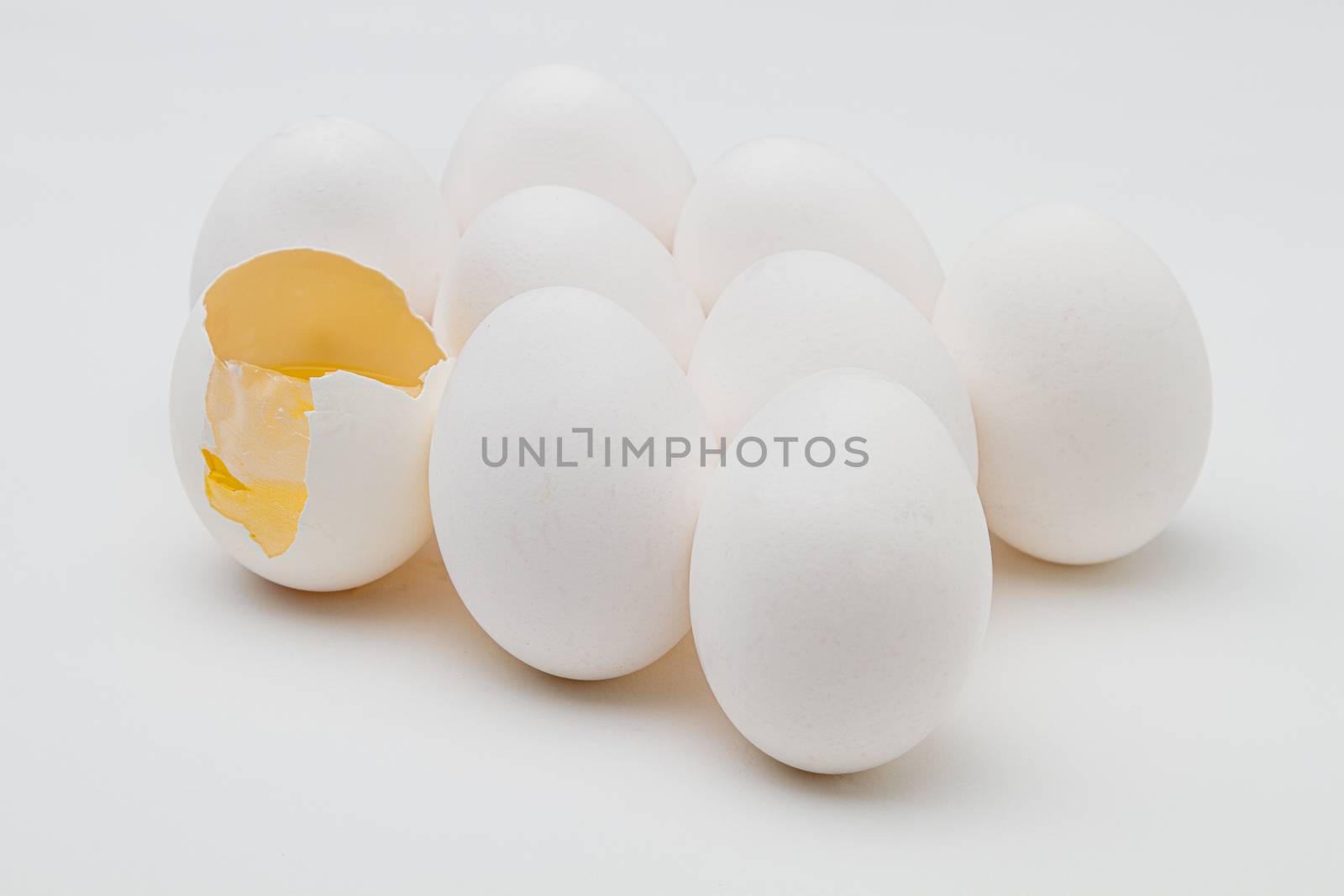group of eggs with one with a broken shell with yoke inside against a white background