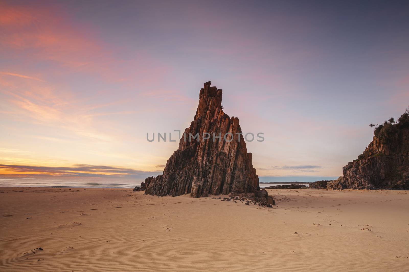 Sunrise morning with pretty red clouds at the remote beach with the local pyramid sea stack rising up out of the sands