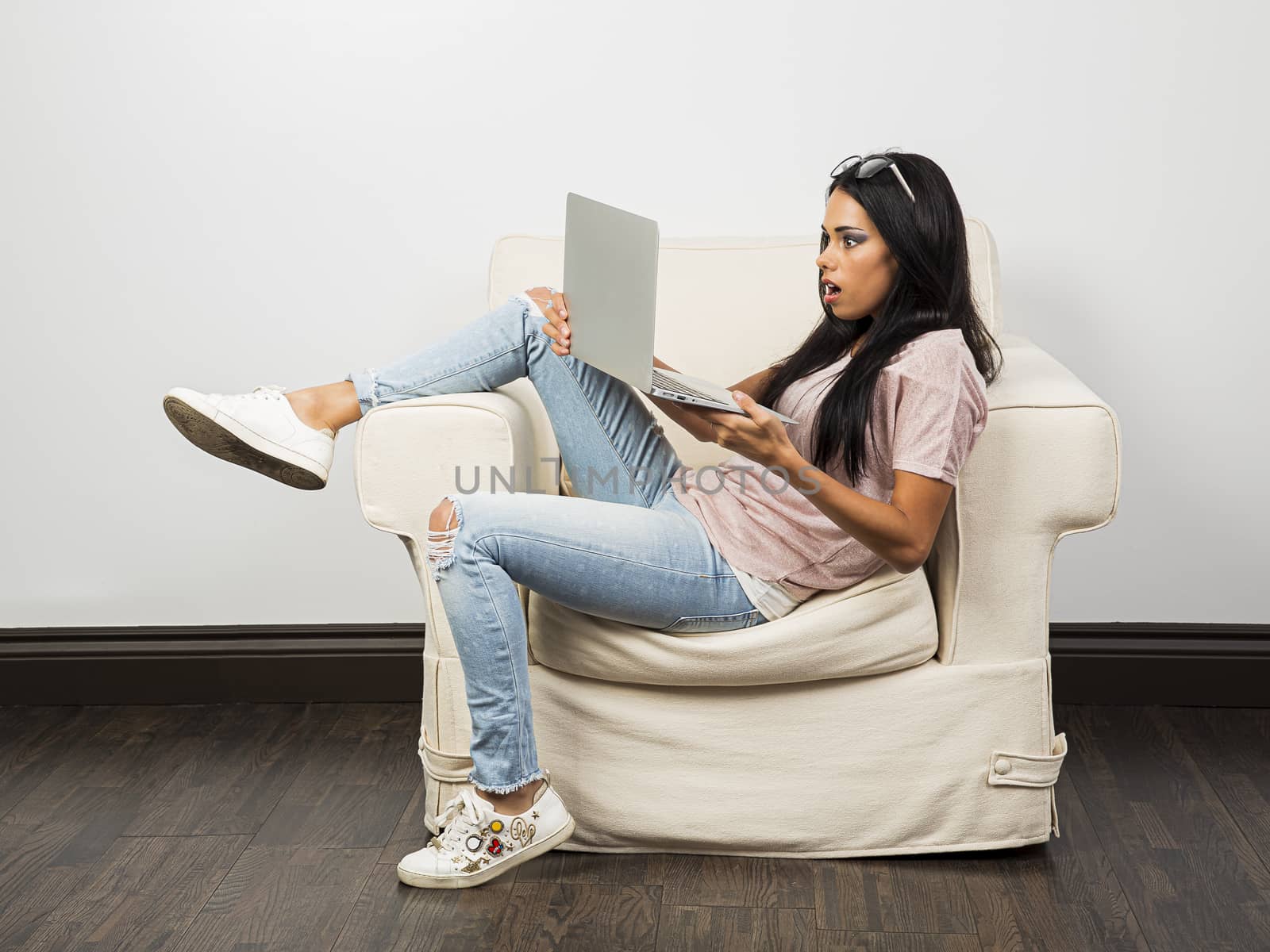 Young woman with her legs up on a couch, with a surprise by what is happening on a laptop screen
