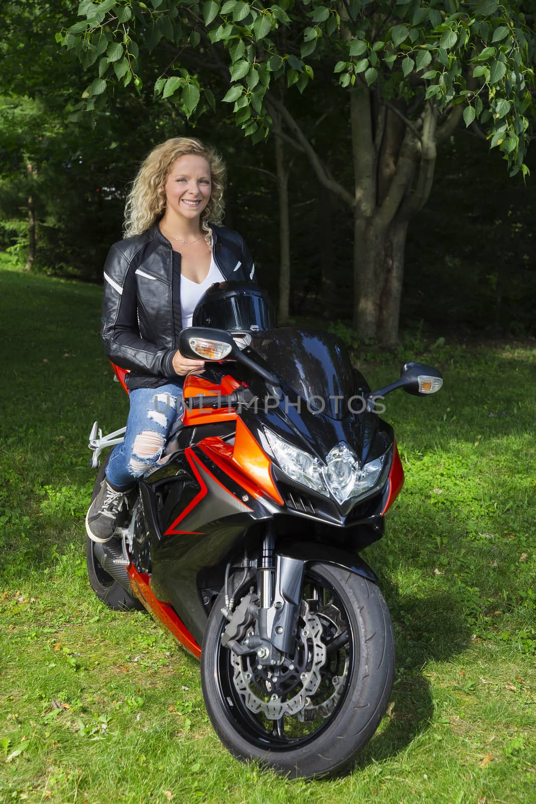 Blond woman, in her twenties, sitting on top of a sport motocycle, in a park