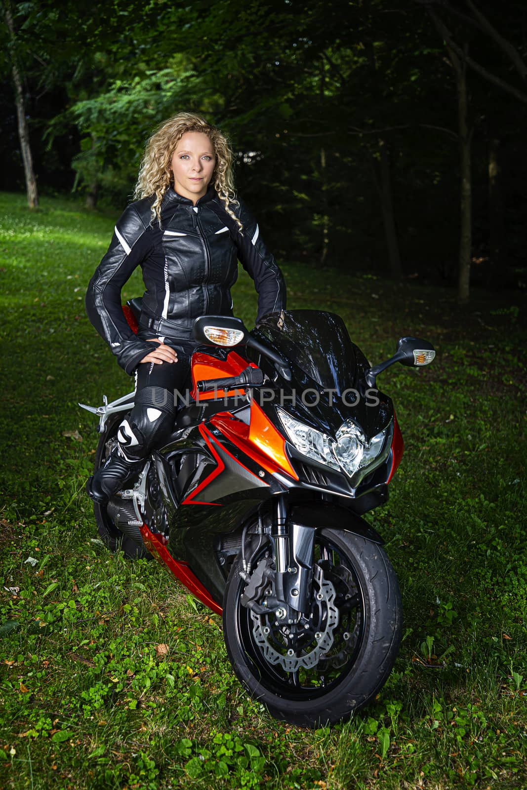 young woman, wearing full motocycle clothes, sitting on a sport motocycle, in a park