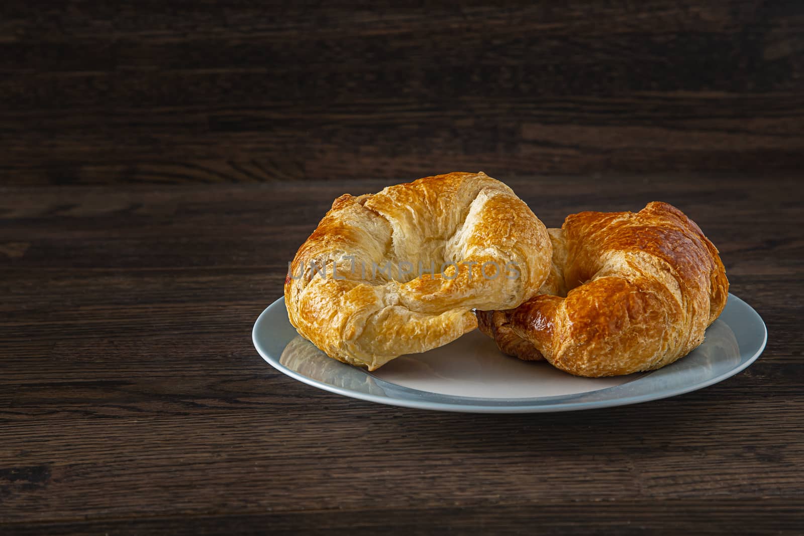 two croissant, stake on top of one another, on a blue rimmed plate against a dark wood background