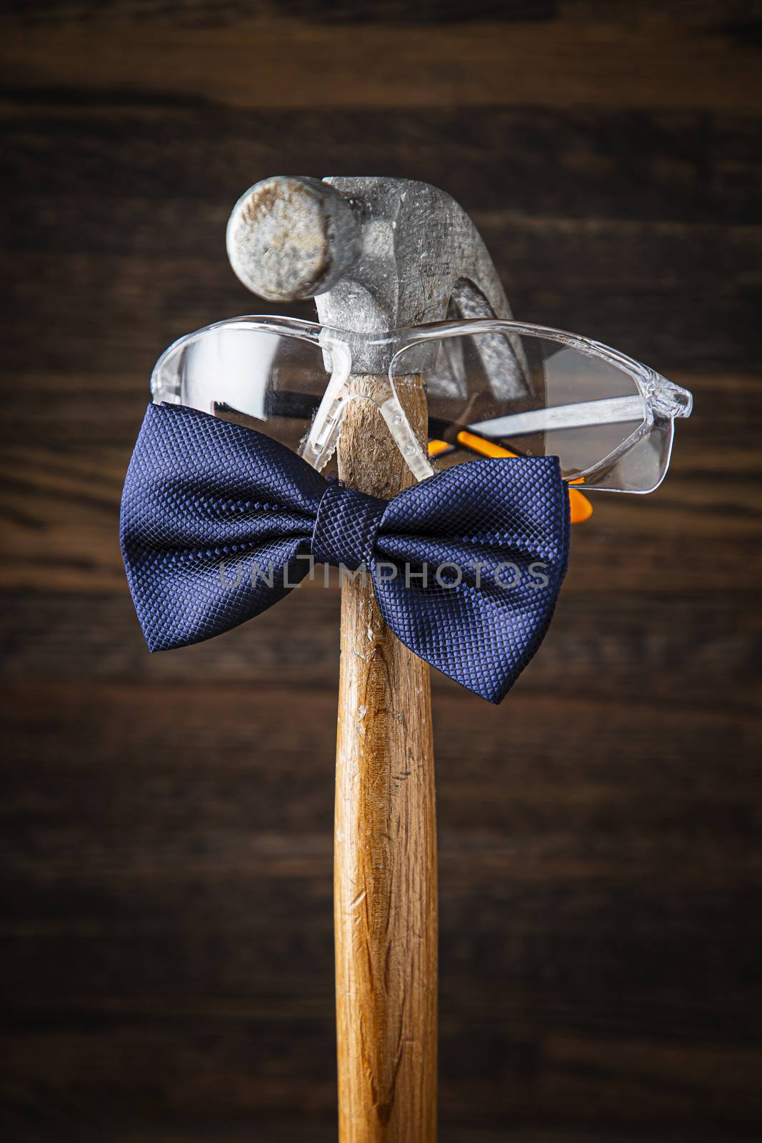 Old weather hammer wearing protective glasses and a blue bowtie against a dark wood background