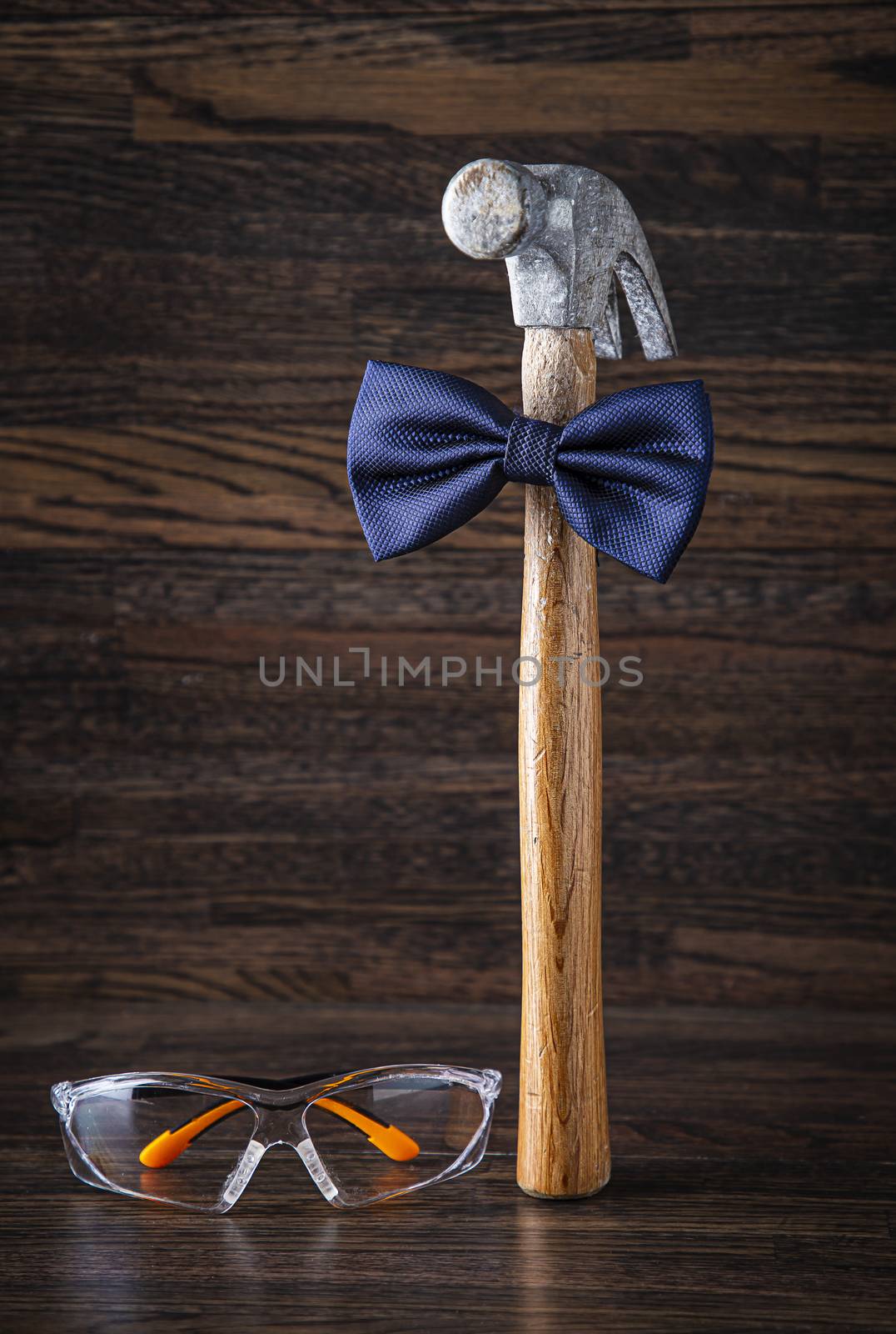 Old weather hammer wearing a blue bowtie, with protective glasses on it’s side against a dark wood background