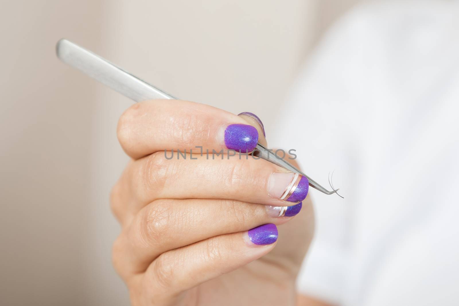 master lash maker is holding one false eyelash by tweezers in hand, close-up