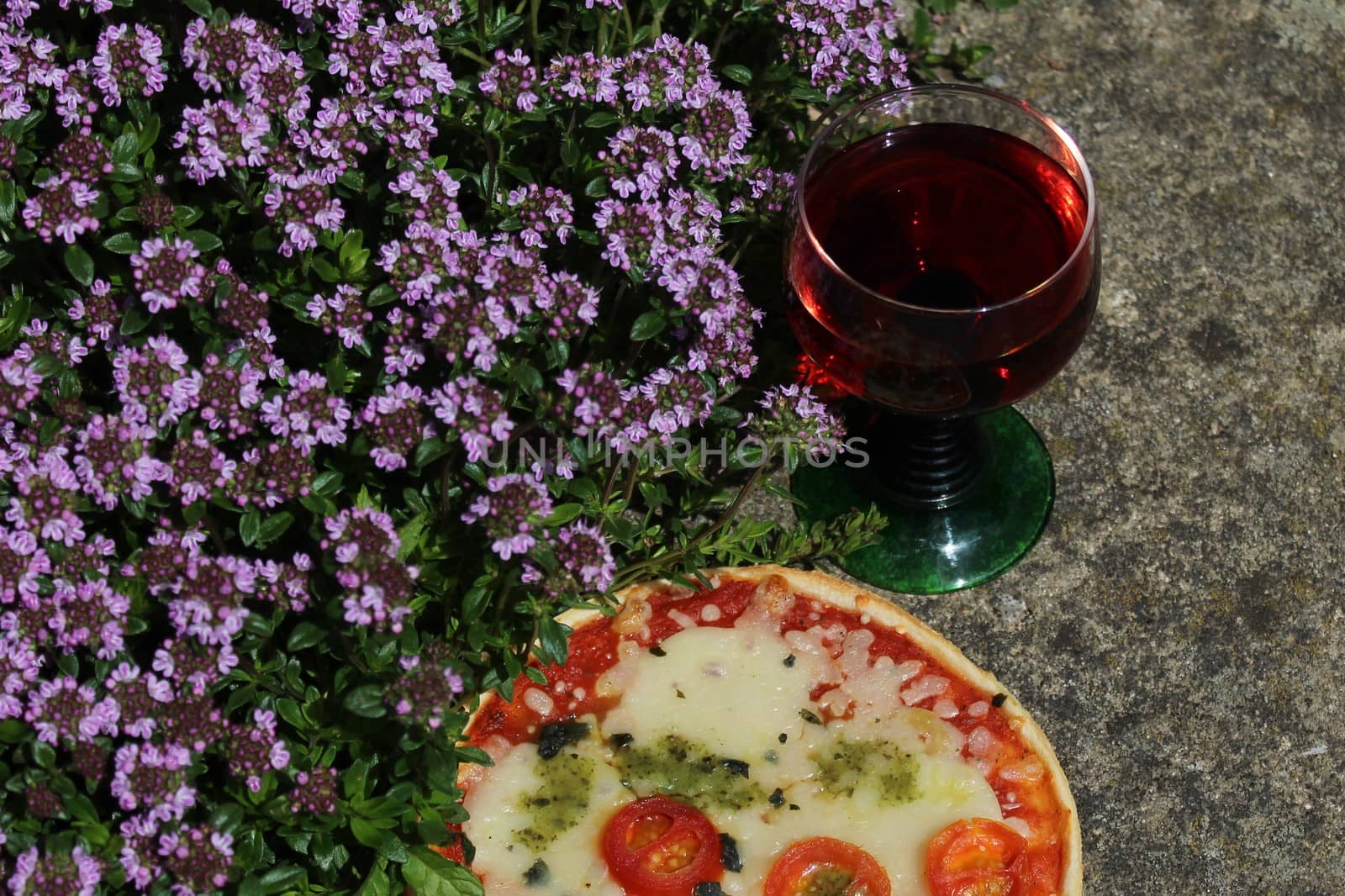 The picture shows pizza and red wine on blossoming thyme