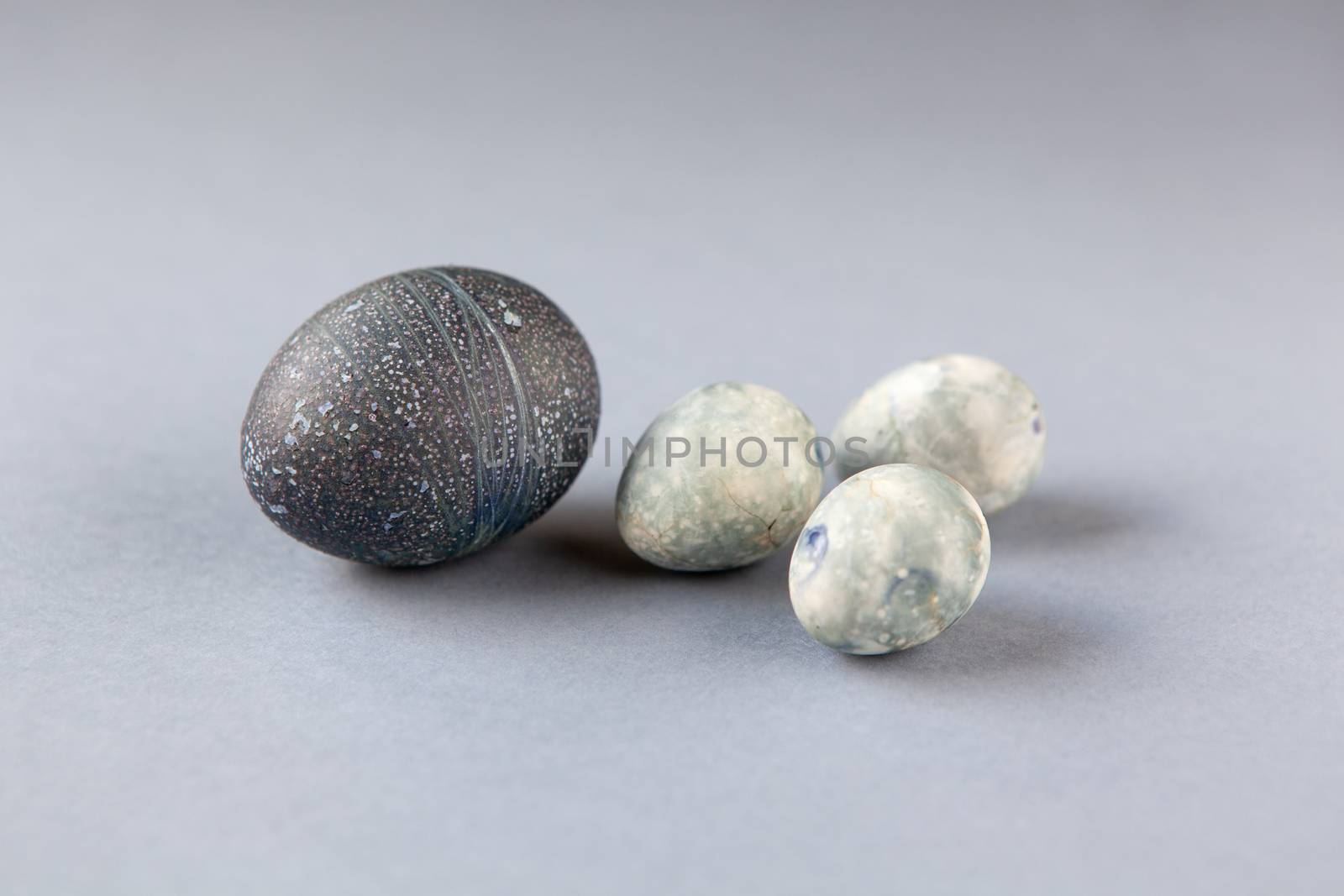 Creatively painted chicken and quail Easter eggs with natural hibiscus dye, look like sea stones on grey background. Happy Easter DIY concept. Soft selective focus. Side view by ALLUNEED