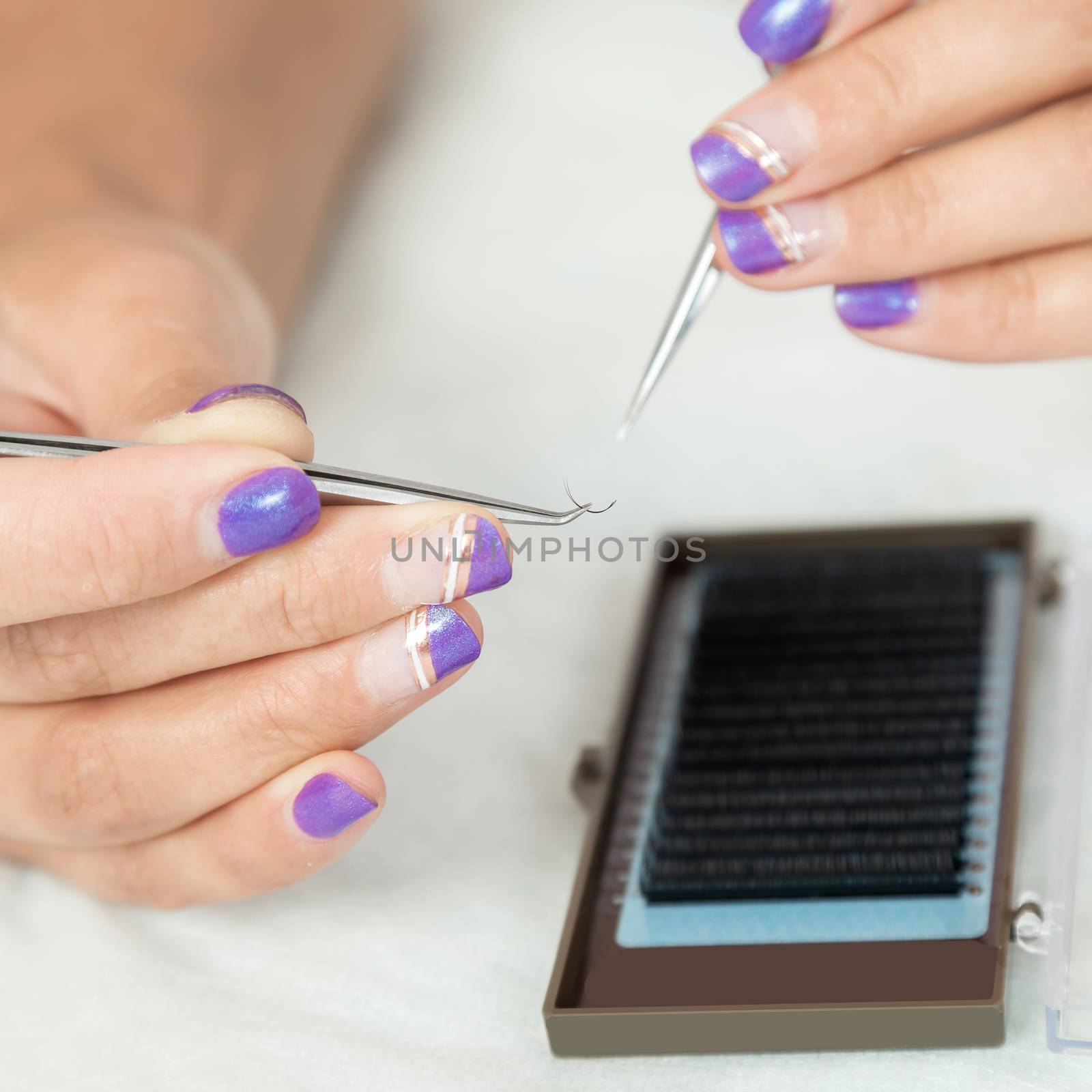 master lash maker is holding one false eyelash by tweezers in hand, close-up