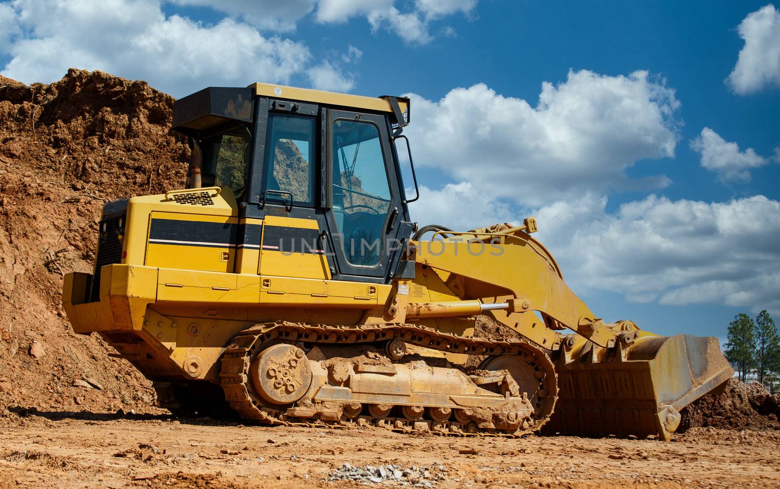 A large, yellow, industrial earth mover by a pile of dirt on a construction site