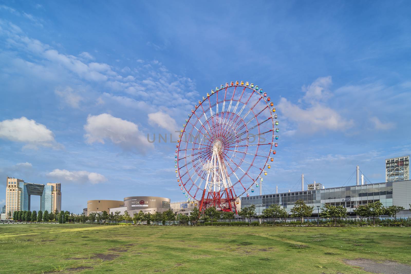 Odaiba colorful tall Palette Town Ferris wheel named Daikanransha visible from the central urban area of Tokyo in the summer blue sky. Passengers can see the Tokyo Tower, the twin-deck Rainbow Bridge, and Haneda Airport, as well as central Tokyo during their ride.