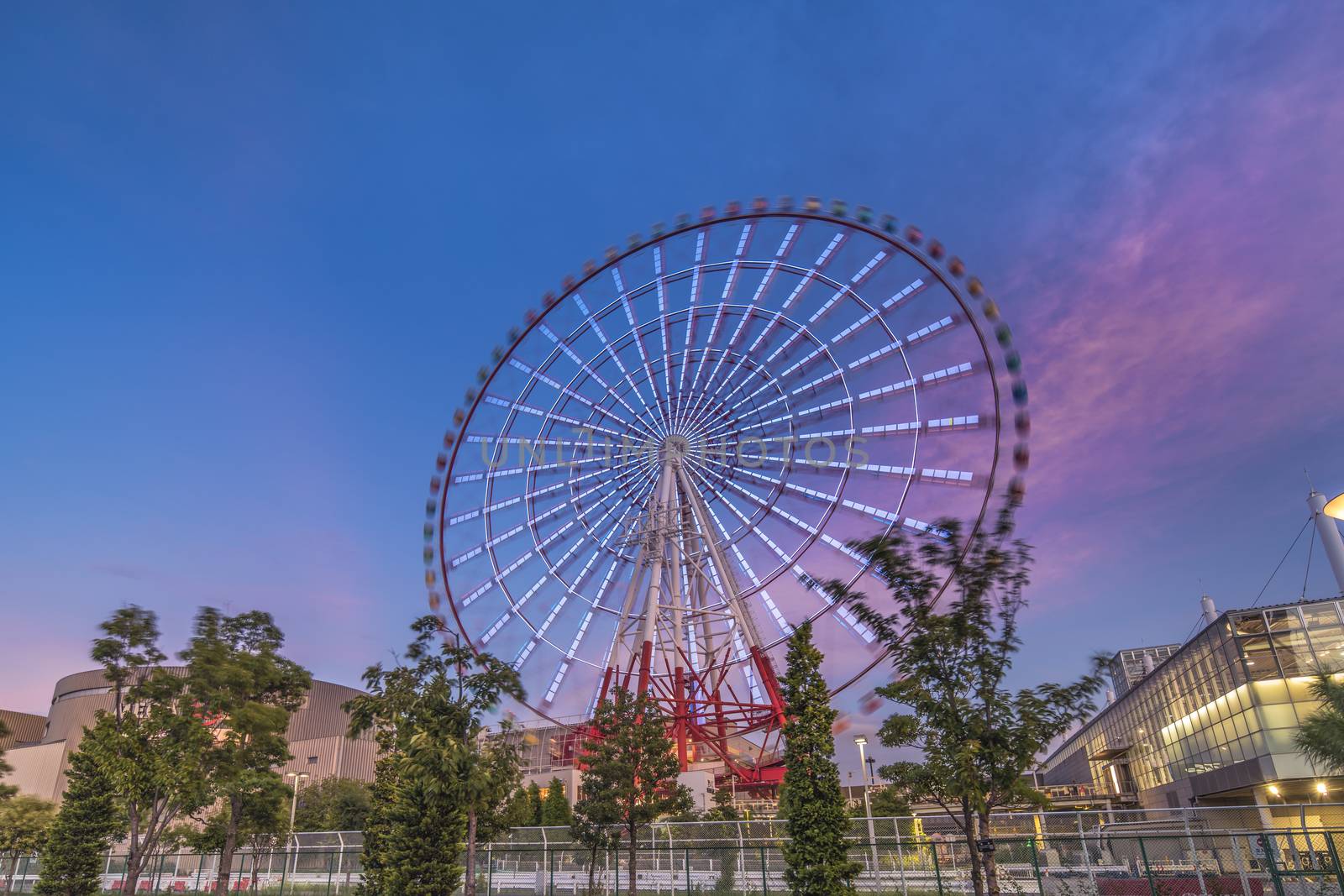 Odaiba colorful tall Palette Town Ferris wheel named Daikanransha visible from the central urban area of Tokyo in the summer sunset purple blue sky. Passengers can see the Tokyo Tower, the twin-deck Rainbow Bridge, and Haneda Airport, as well as central Tokyo during their ride.