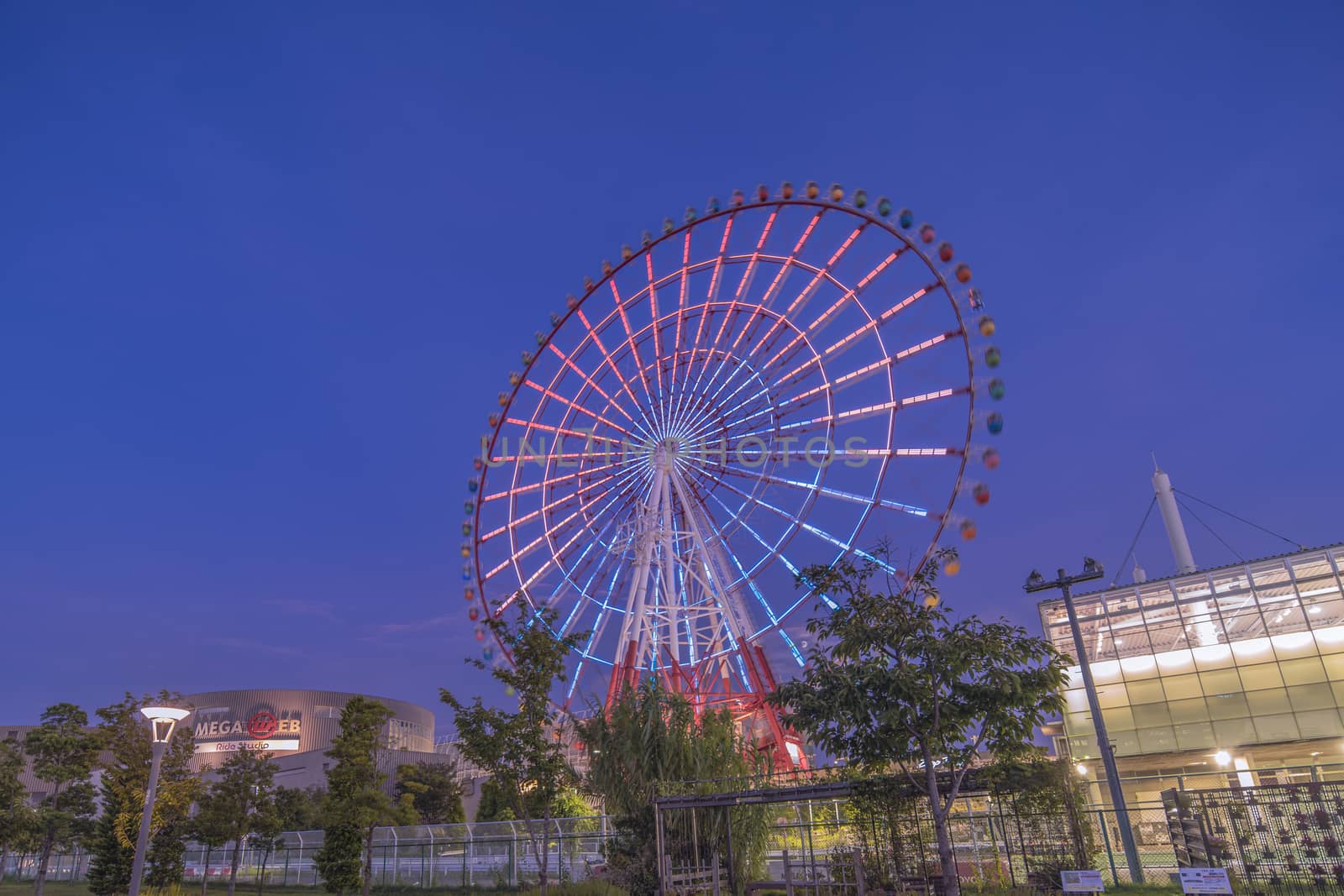 Odaiba colorful tall Palette Town Ferris wheel named Daikanransha visible from the central urban area of Tokyo in the summer sunset purple blue sky. Passengers can see the Tokyo Tower, the twin-deck Rainbow Bridge, and Haneda Airport, as well as central Tokyo during their ride.