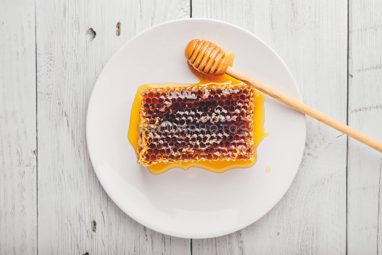 Top view of delicious yummy honeycomb on bright plate with honey dipper over light wooden background