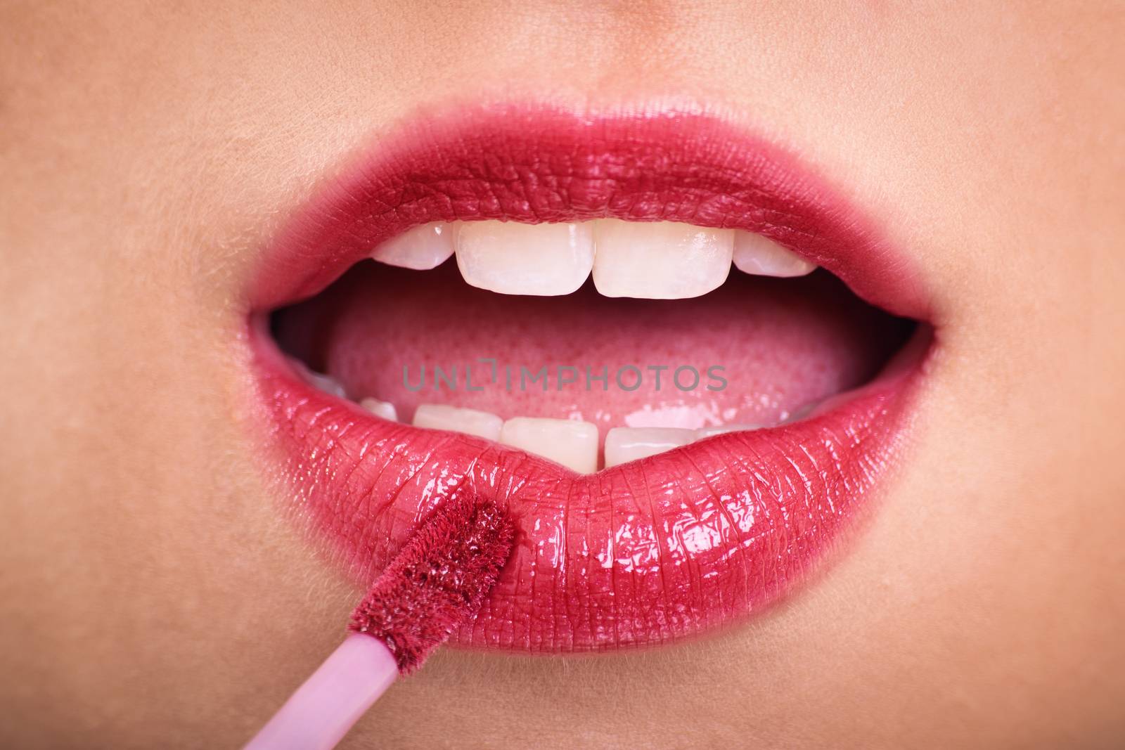 Cosmetics, makeup and skin care concept. Close up of woman applying lipstick or lip gloss to her plump pink lips.