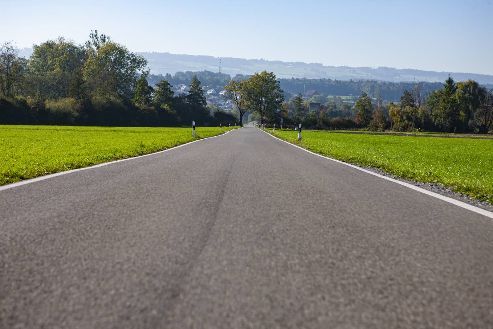 country road leading into horizon during daylight with hills in background with trees and green grass