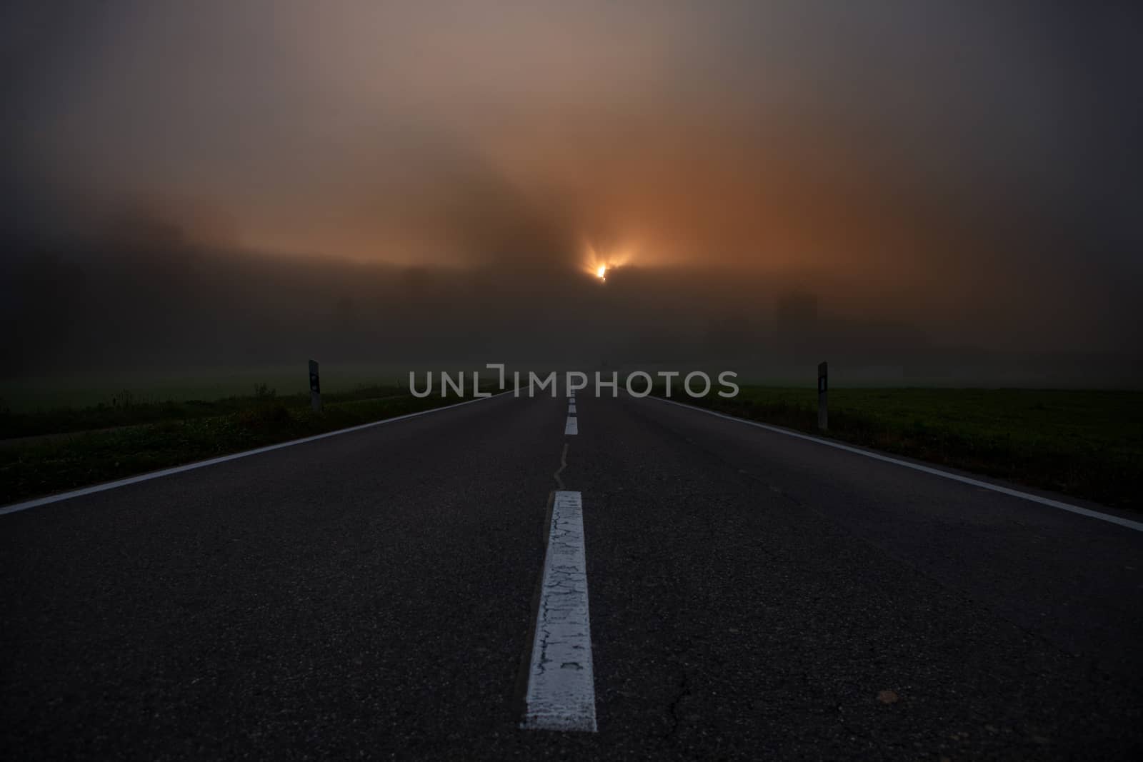 road towards horizon during sunrise with fog. Showing white middle line and dark hill