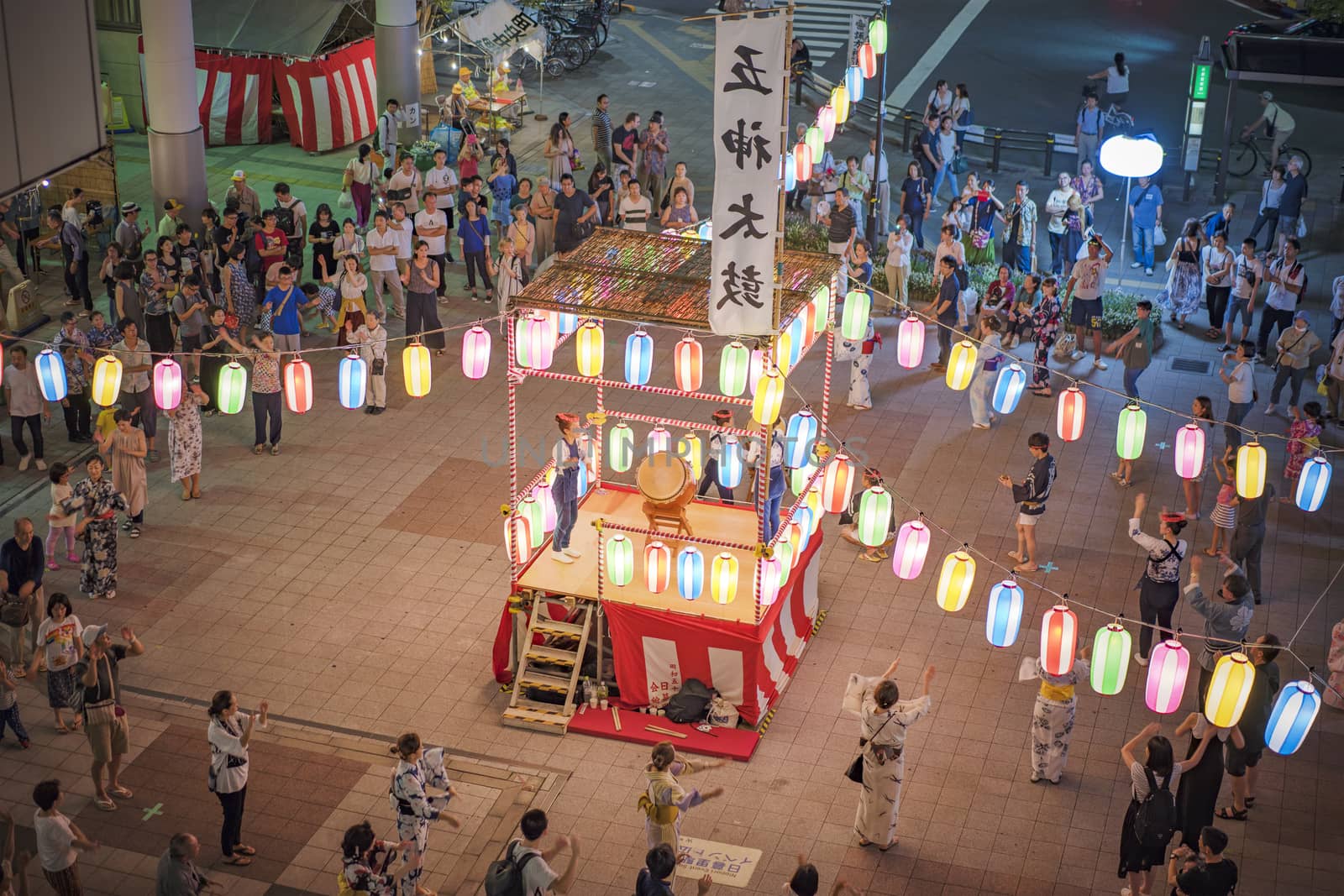 View of the square in front of the Nippori train station decorated for the Obon festival with illuminated paper lanterns  in the summer night with a yagura tower and paper lanterns in the Arakawa district of Tokyo.