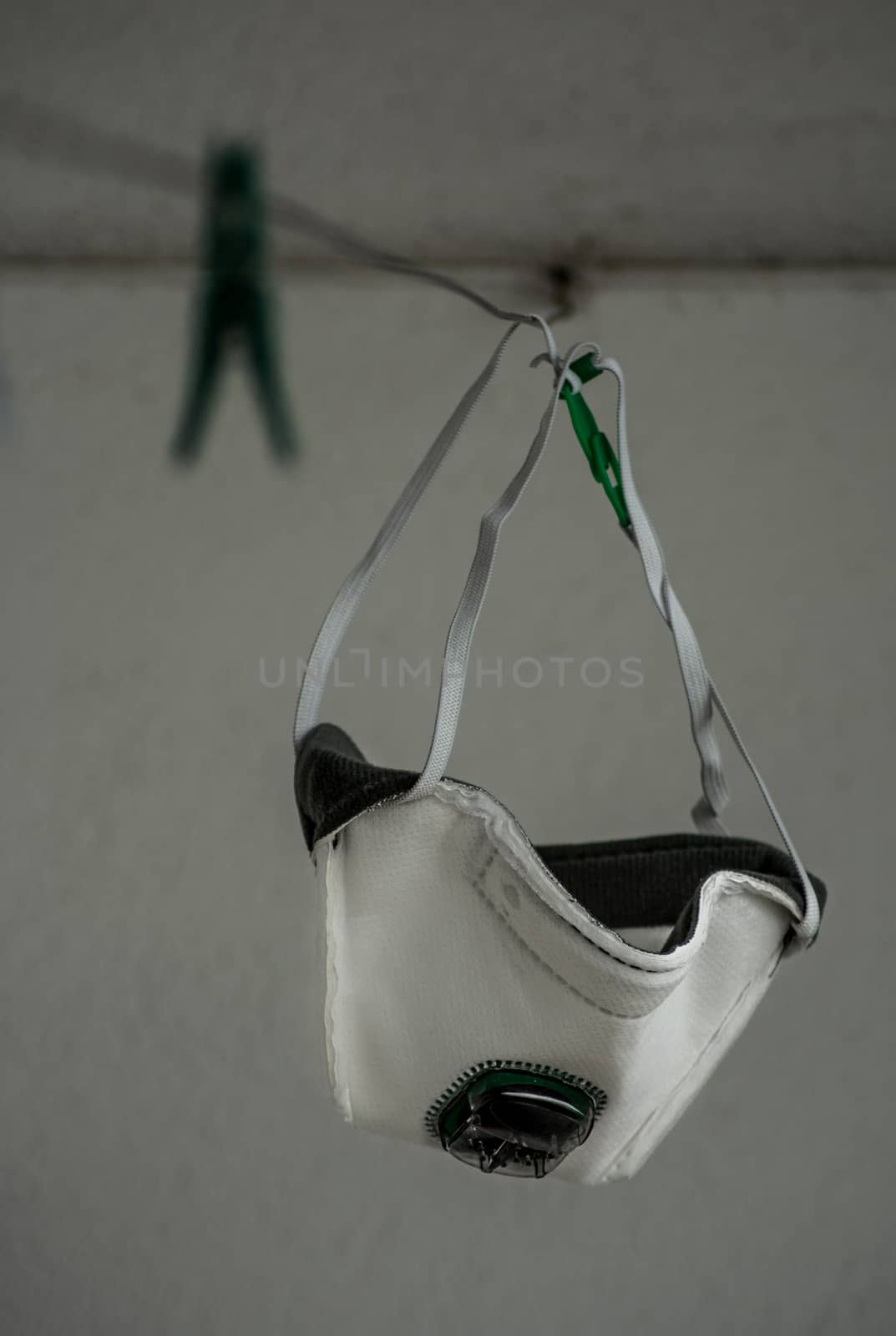 A white medical mask with green air filter hanging on a clothesline. by justbrotography