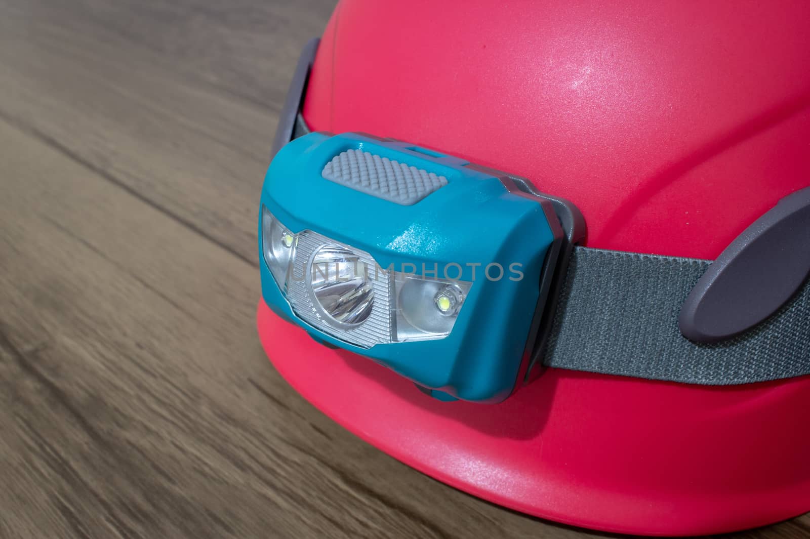 Teal led headlamp turned off strapped to a pink climbing helmet on a wooden table