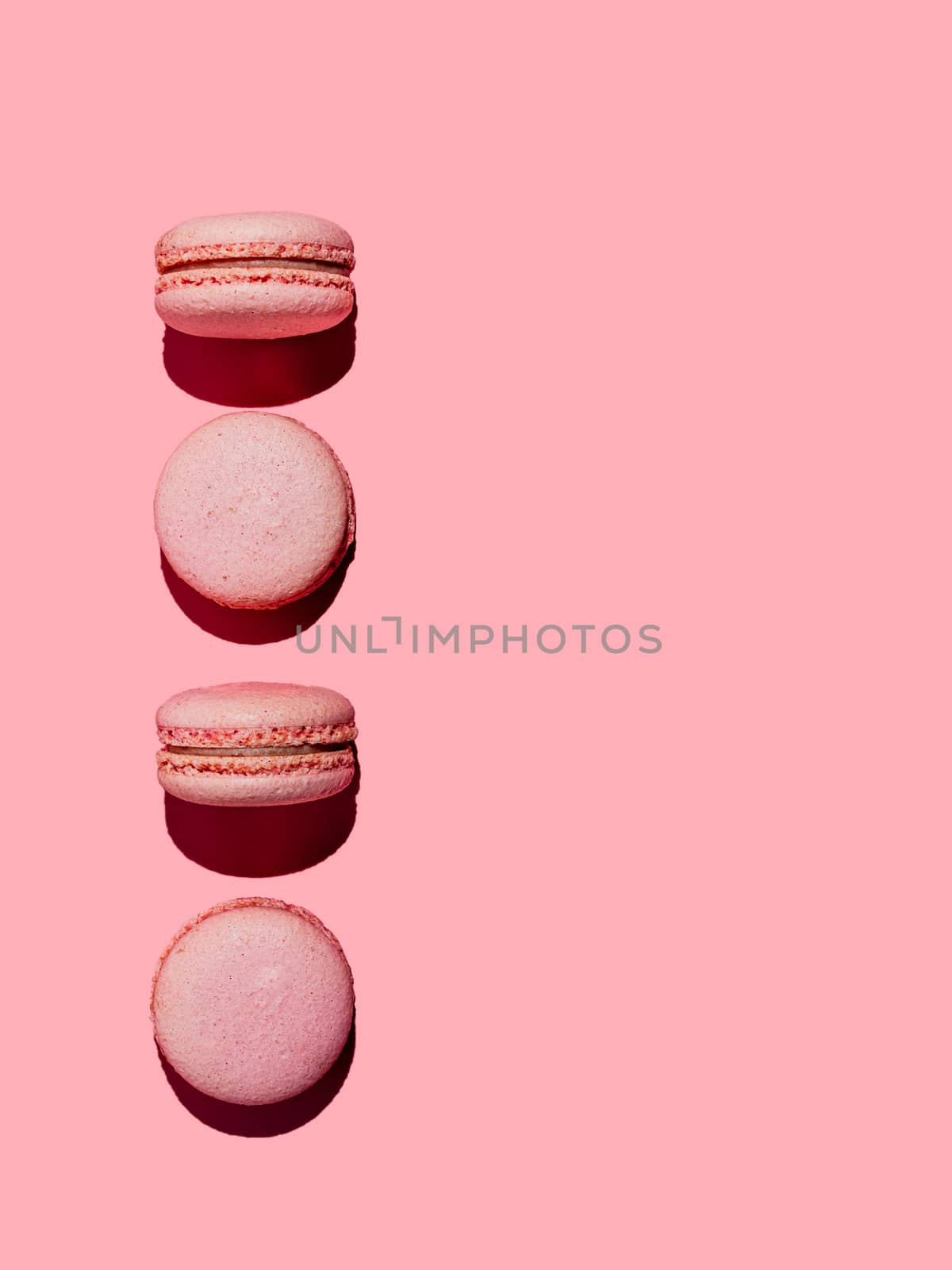 Pink macarons with copy space. Row of perfect french macarons or macaroons on pink background. Top view or flat lay. Hard light