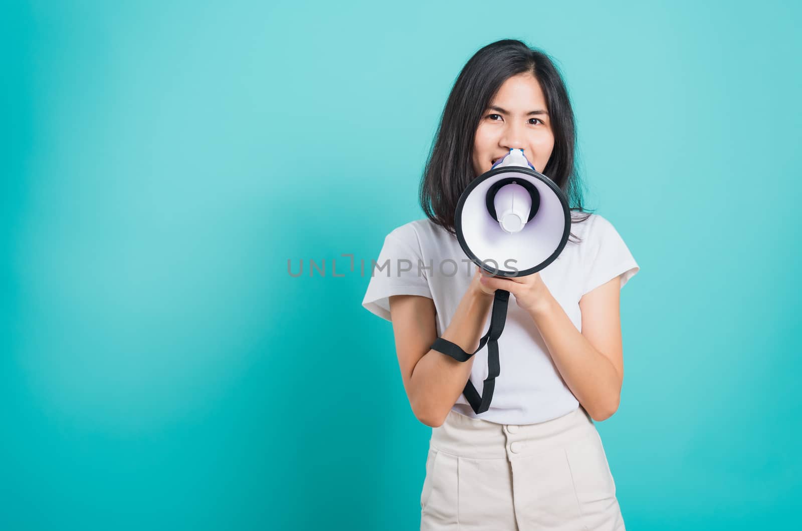 Portrait Asian beautiful young woman standing smile holding and shouting into megaphone looking to camera, shoot the photo in a studio on a blue background, There was copy space
