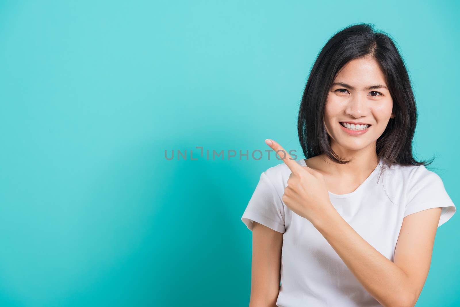 Portrait Asian beautiful young woman wearing white T-shirt standing smile white teeth, She pointing finger up and looking at camera, shoot photo in studio on blue background, There was copy space.