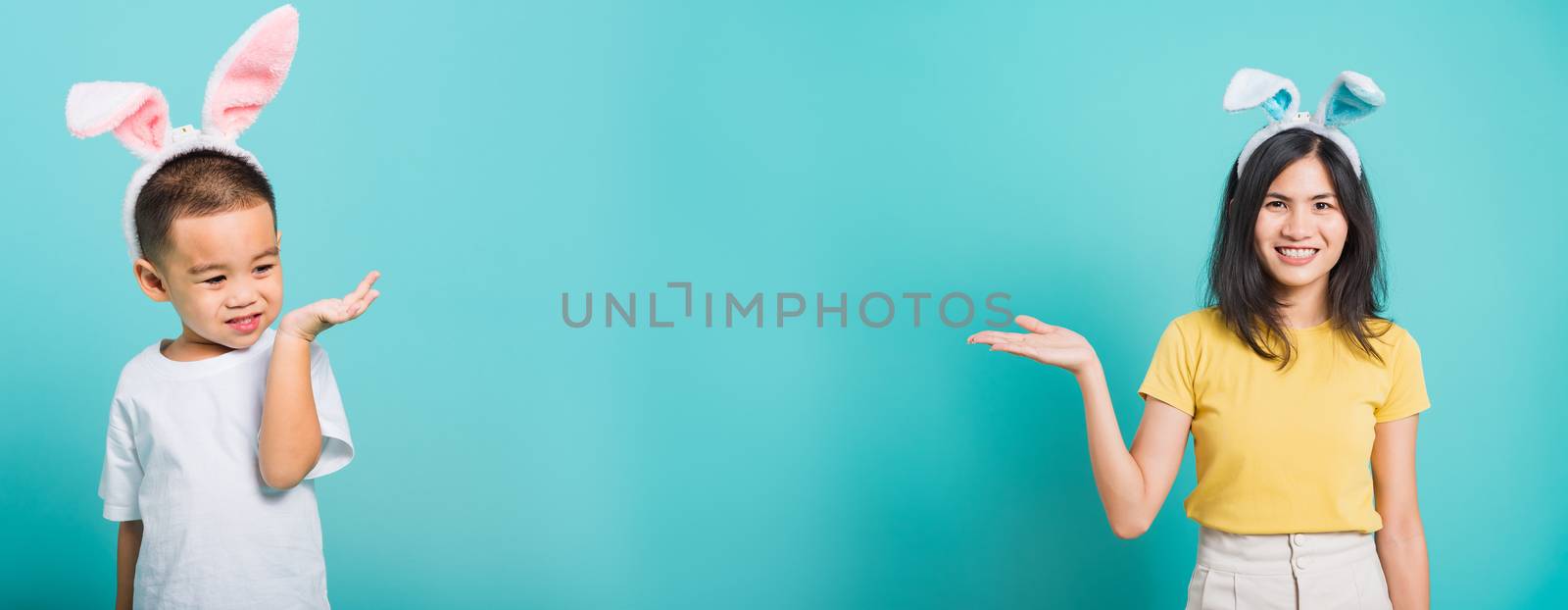Portrait happy Asian young beautiful woman and children smile standing so happy in rabbit ears show something on hand, studio shot on blue background with copy space, Easter day concept