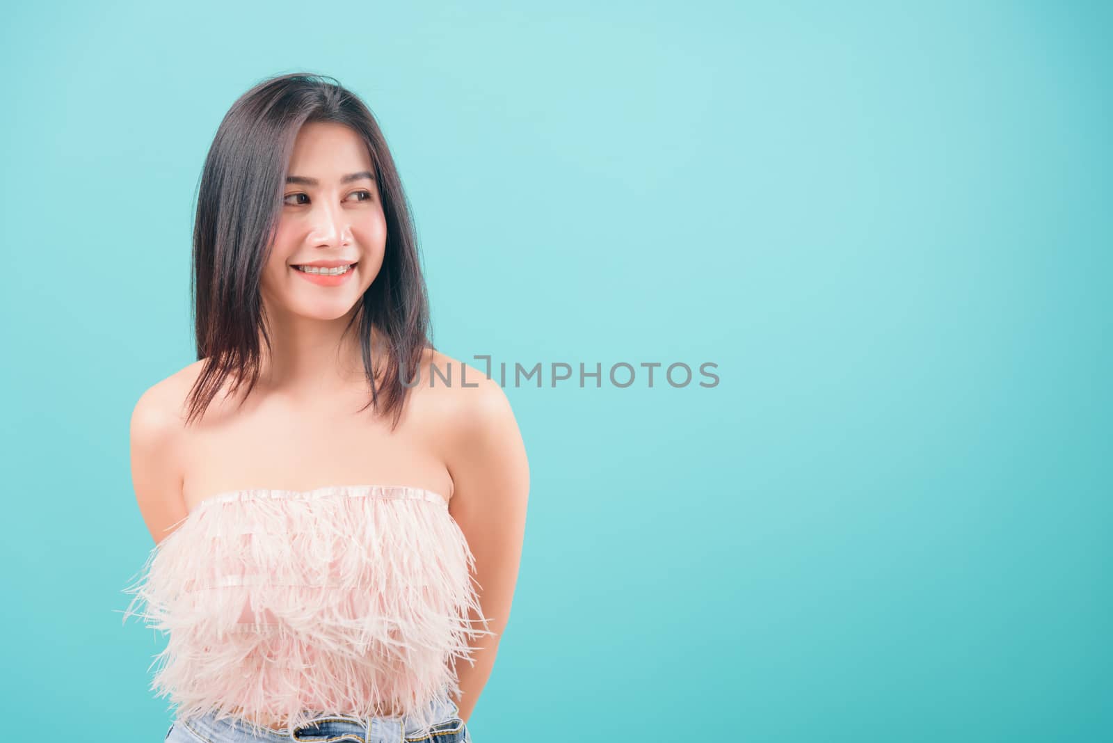 Asian happy portrait beautiful young woman standing her looking out side and looking to side isolated on blue background with copy space for text