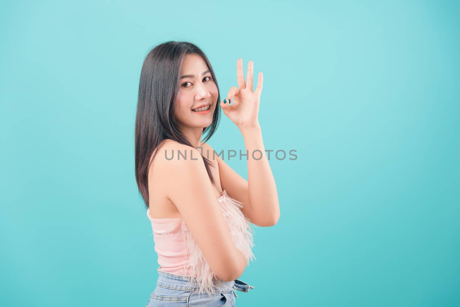 Asian happy portrait beautiful young woman standing smiling her show finger OK sign and looking to camera isolated on blue background with copy space for text