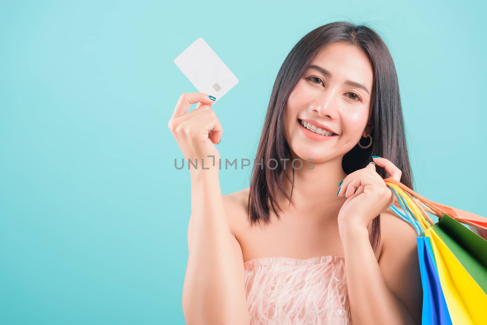 Asian happy portrait beautiful young woman standing smile in summer shopping holding credit card and multicolor shopping bags on hand and looking to camera on blue background with copy space for text
