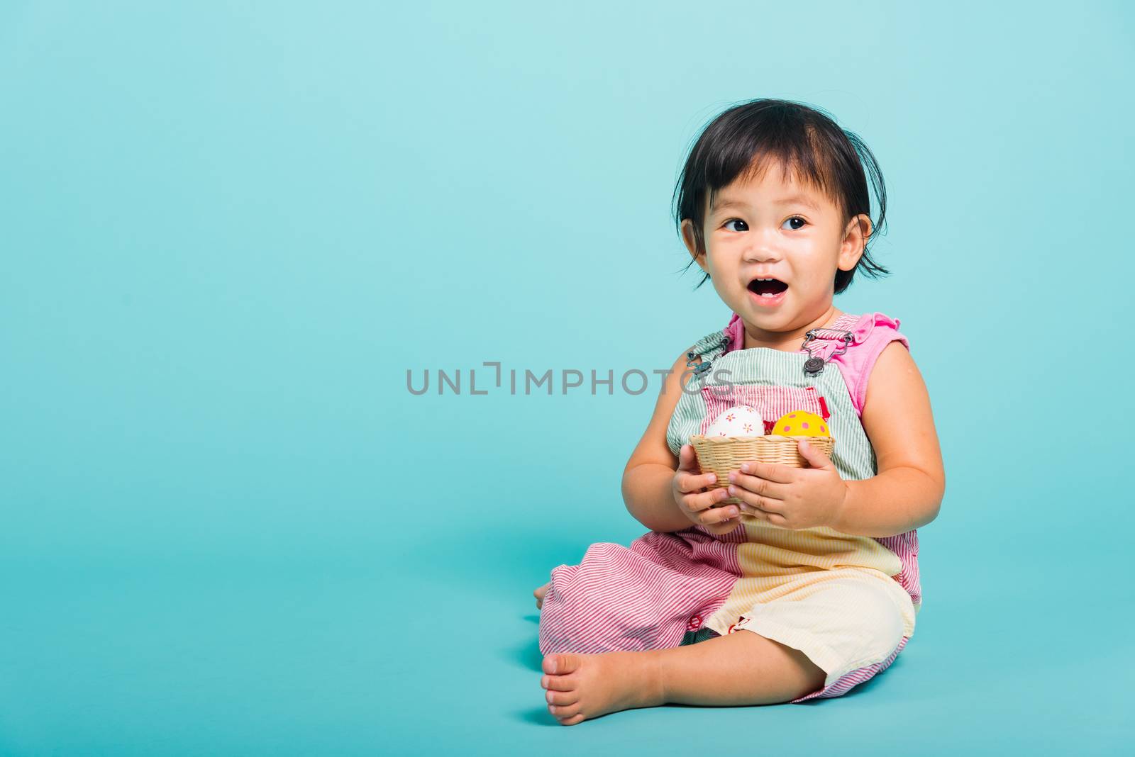 Asian Cute little baby girl beautiful holding Easter egg in basket, studio shot on blue background with copy space, Easter day concept