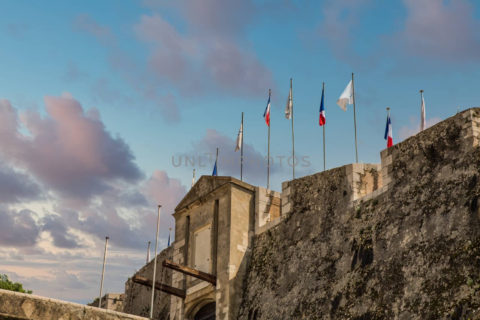 Flags in calm wind over a stone fortress under clear blue skies