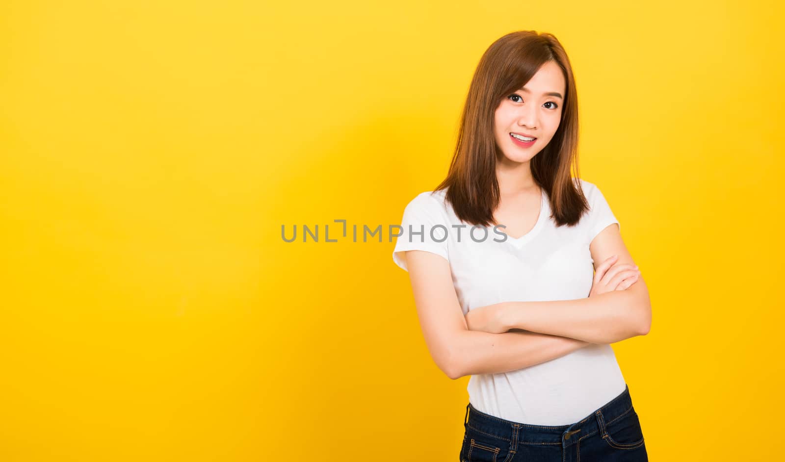 Asian happy portrait beautiful cute young woman teen standing wear t-shirt smile her confidence with crossed arms looking to camera isolated, studio shot on yellow background with banner copy space