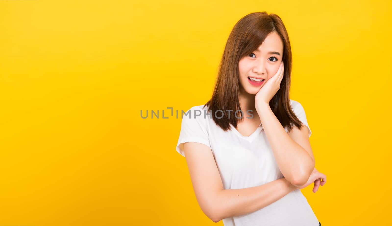 Asian happy portrait beautiful cute young woman teen standing wear white t-shirt posting rest chin on hand looking to camera isolated, studio shot on yellow background with copy space for text