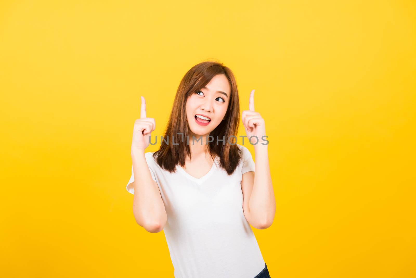 Asian happy portrait beautiful cute young woman teen standing wear t-shirt makes gesture two fingers point upwards above looking to camera isolated, studio shot on yellow background with copy space