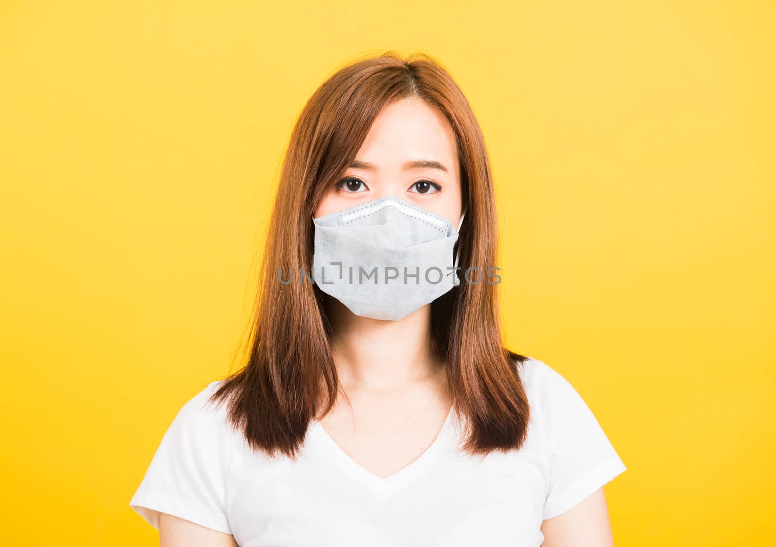 Asian happy portrait beautiful cute young woman standing wear t-shirt making mask protection from virus epidemic or air pollution looking camera isolated, studio shot yellow background with copy space