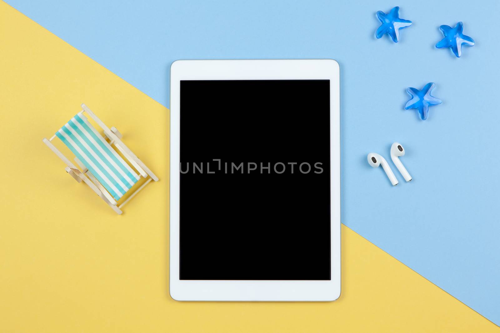 Tablet, wireless headphones, deck chair on yellow and blue background, starfishes, copy space, flat lay. Working space of freelancer. Freelance, planning of vacation, travel concept. Horizontal by ALLUNEED