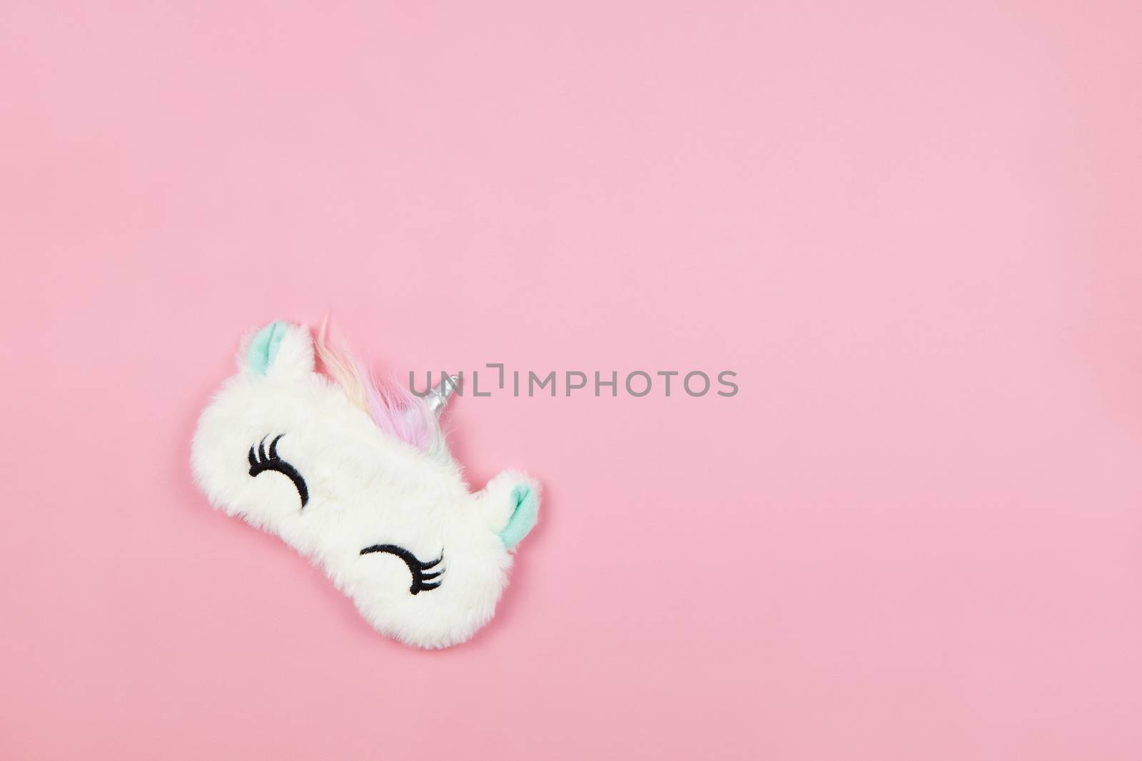 White fluffy fur sleep mask unicorn with closed eyes and small ears on pastel pink paper background, copy space. Top view, flat lay. Concept of vivid dreams. Accessories for girls and young women by ALLUNEED